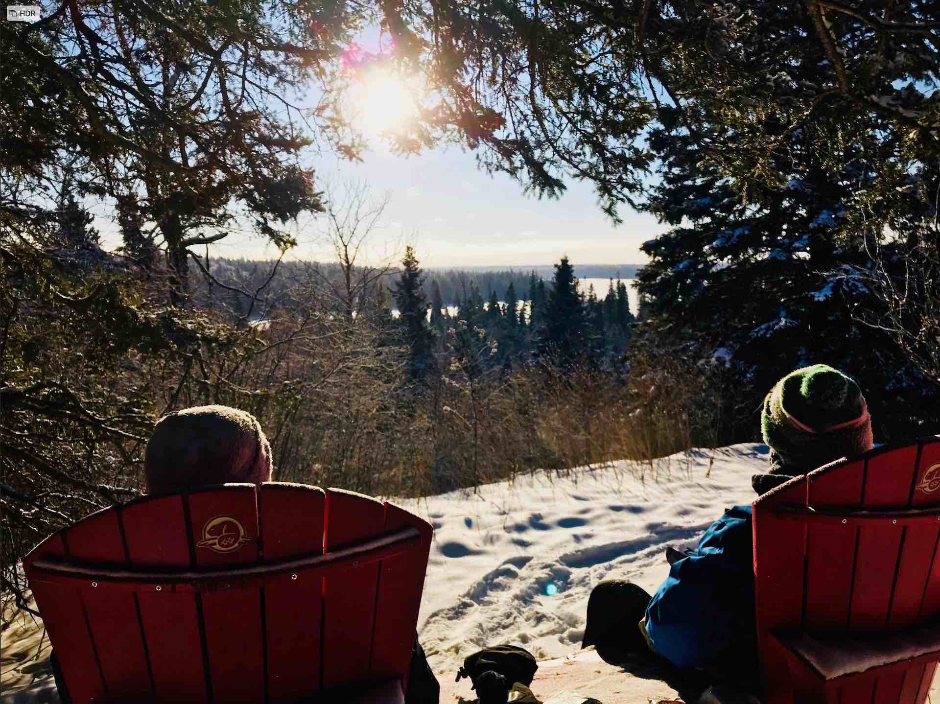 Photograph of two people in red chairs overlooking a frozen lake.